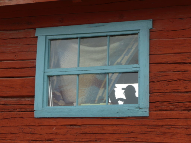 Siluett av man som meckar med en motorcykel genom ett fönster på en stuga vid Molnsätra Gård